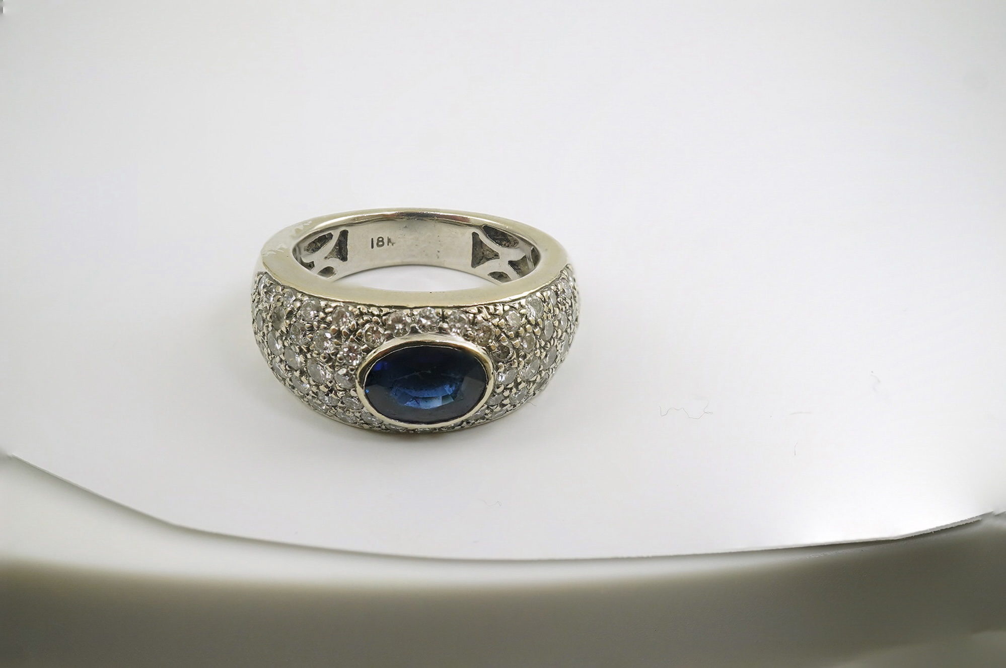 A modern 18k white gold and gypsy set single stone oval cut sapphire set ring, with pave diamond set shoulders